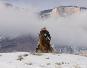 Flitner Ranch, Shell, WY, horses in winter, cowboy riding over hill in snow