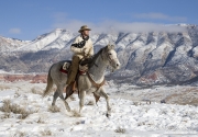 cowboy on grey Quarter horse trotting in the snow at Flitner Ranch, Shell, WY