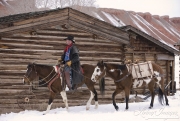 Flitner Ranch, Shell, WY, horses in winter, cowboy leading pack horse next to cabin in snow